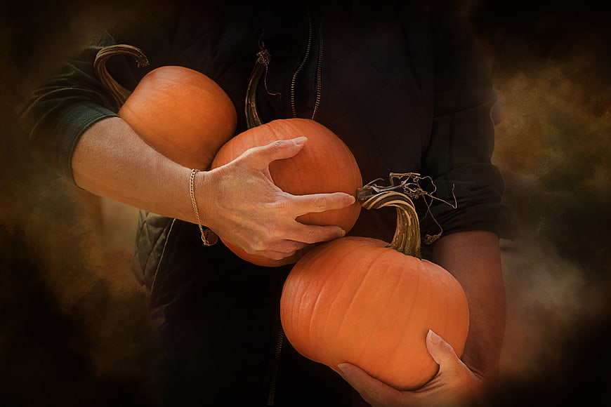 Woman holding three orange pumpkins in autumn