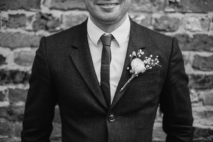 Black and white groom portrait with boutonniere against brick wall