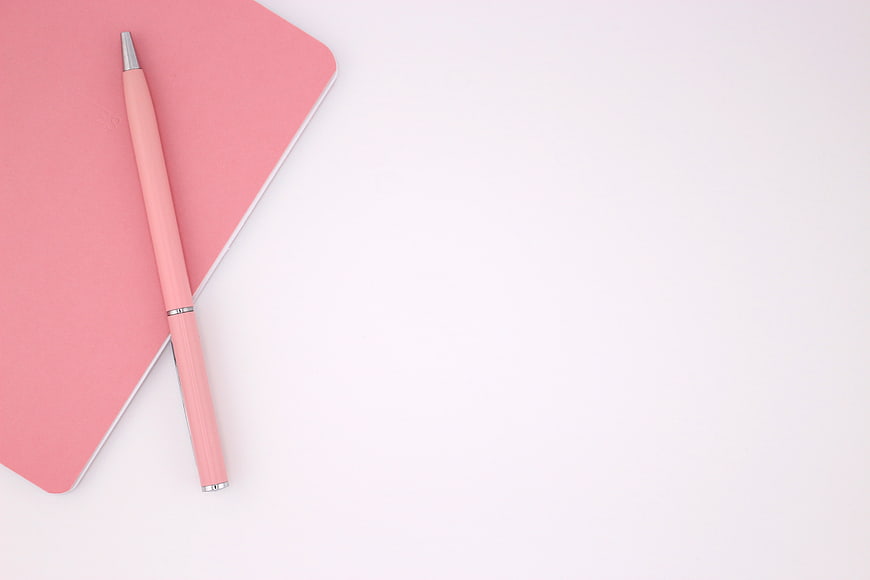 Minimalist pink notebook and pen on white background