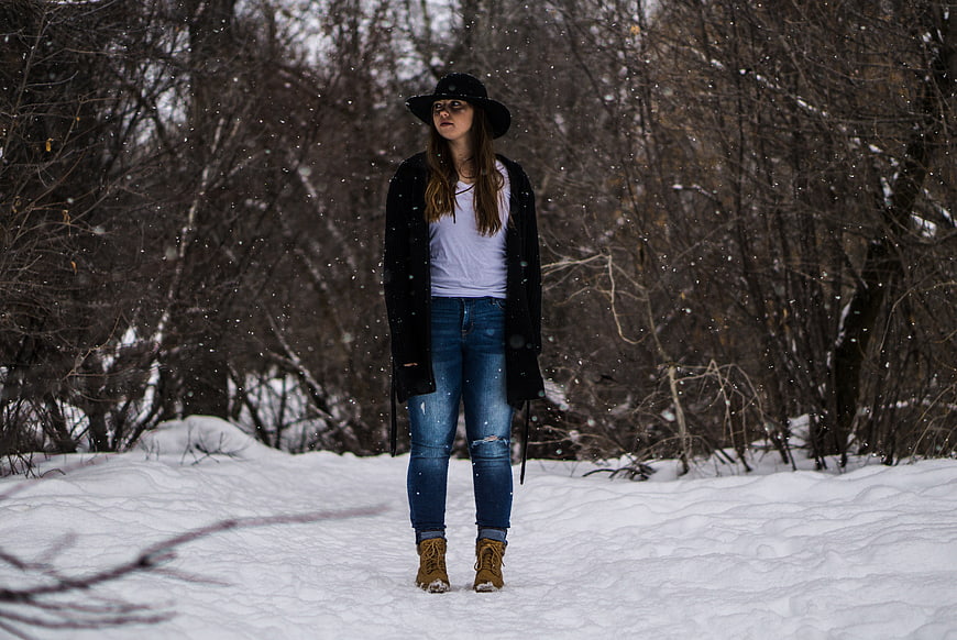 Young woman in black hat standing in snowy winter forest