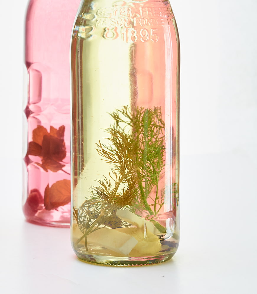 Infused Vodka Bottles with Herbs and Flowers on White Background