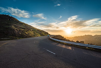 Runner on winding road at sunset with dramatic sky