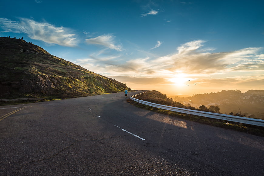 Runner on winding road at sunset with dramatic sky