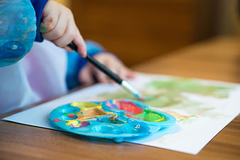 Close-up of a child's hand painting with a brush and colorful palette