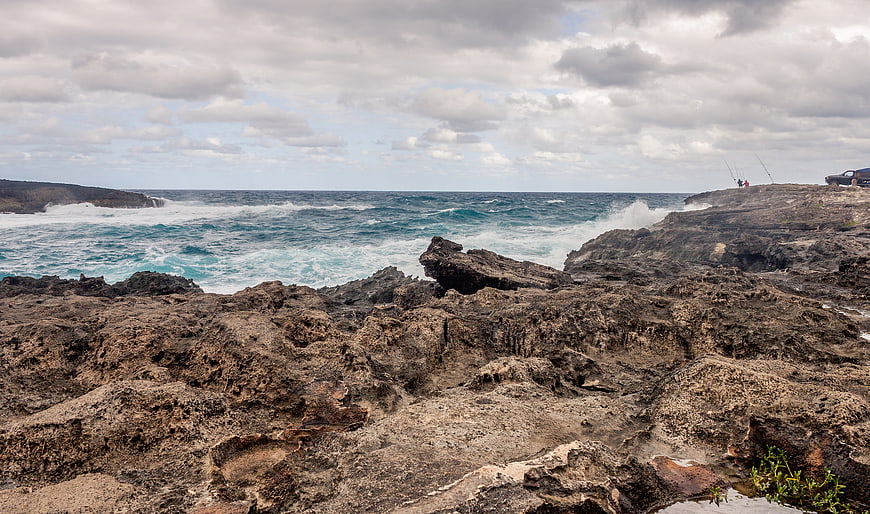 Rugged volcanic coastline with crashing waves and distant fishermen