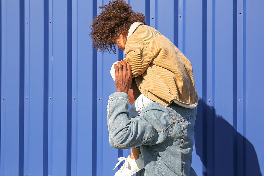 Father carrying daughter on shoulders against blue wall