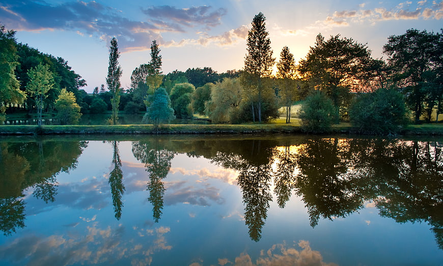 Serene Lake Reflection at Sunset with Trees and Clouds