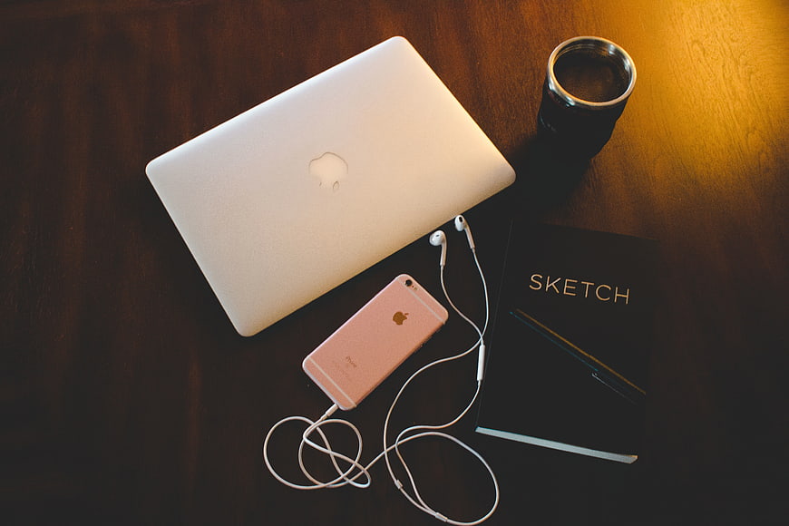 Flat lay of laptop, smartphone, sketchbook, and coffee on wooden desk