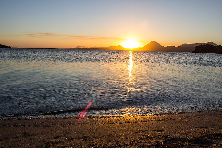 Serene Sunset Over Calm Water with Distant Mountains