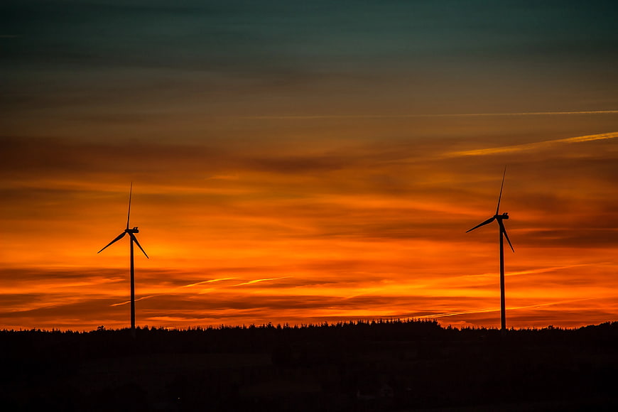 Wind Turbines Silhouette Against Vibrant Orange Sunset Sky