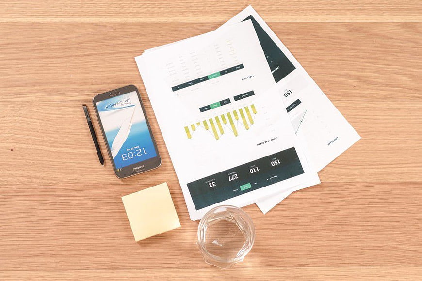 Flat lay of smartphone, business charts, and office supplies on wooden desk