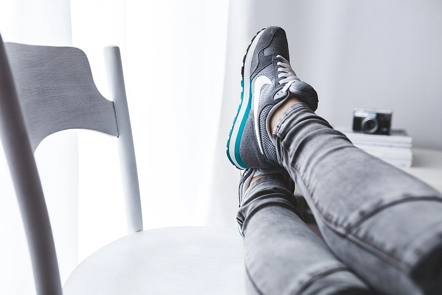 Woman resting legs in sneakers on white chair