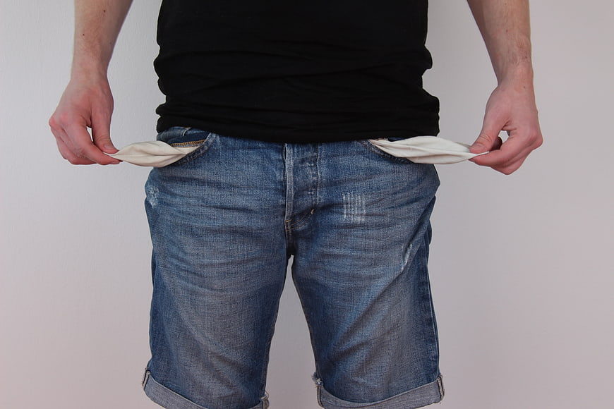 Man turning out empty pockets in jeans symbolizing poverty