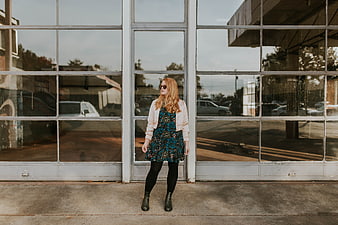 Woman in floral dress and sunglasses standing by glass windows