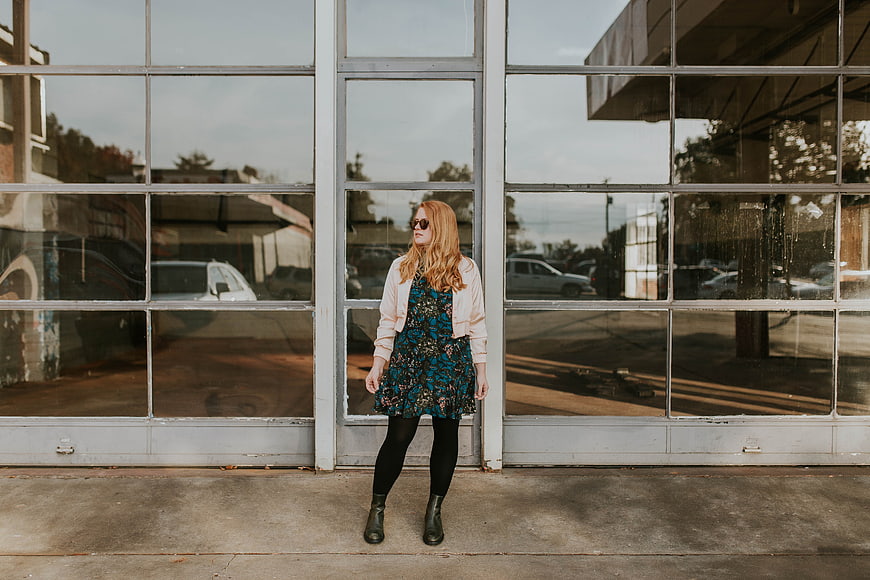 Woman in floral dress and sunglasses standing by glass windows