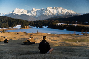 Man meditating in meadow with snowy mountains and frozen lake