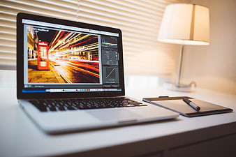Laptop displaying photo editing software with graphics tablet on desk