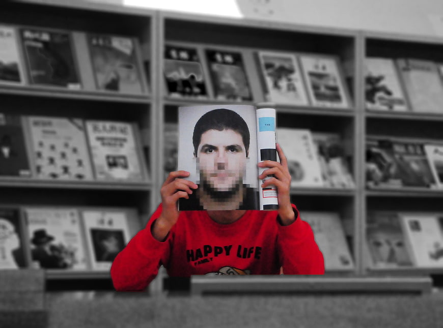 Man holding magazine with pixelated face in library