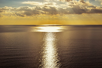 Golden sunset over calm ocean with sunbeams and sparkling water reflection