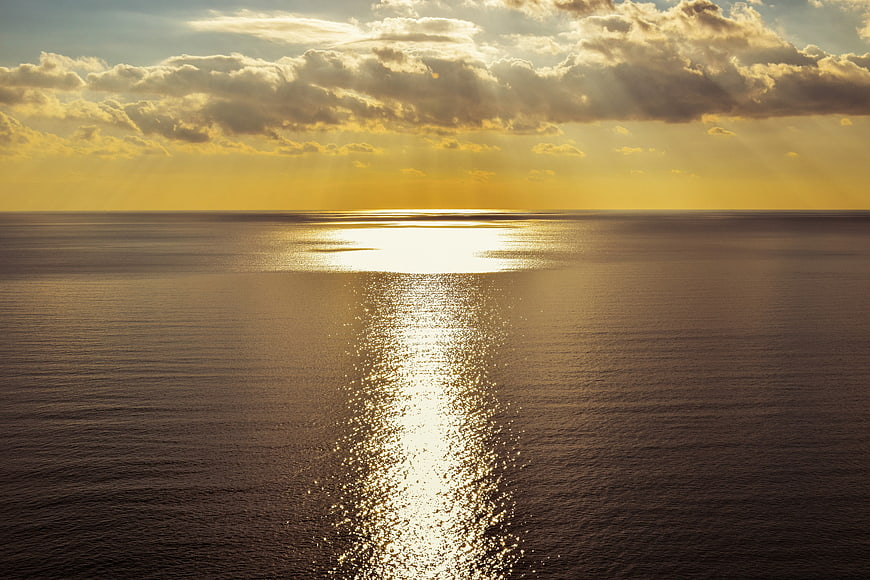 Golden sunset over calm ocean with sunbeams and sparkling water reflection