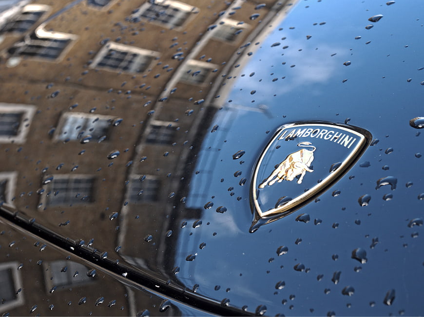 Lamborghini badge on blue car with raindrops and building reflection