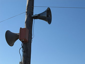 Two loudspeakers mounted on a wooden utility pole against a clear blue sky