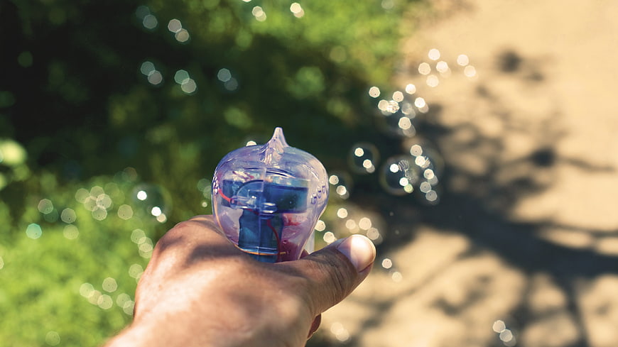 Hand holding bubble blower with floating bubbles in nature