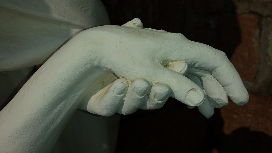 Close-up of white stone hands clasped together in prayer