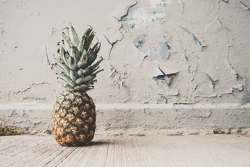 Whole pineapple on wooden surface against distressed wall