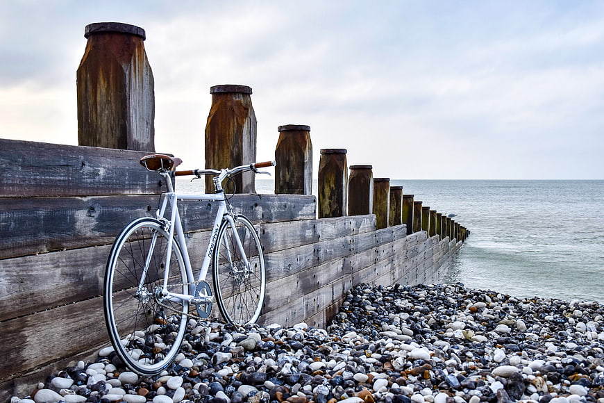 White Bicycle Leaning Against Wooden Seawall on Pebble Beach