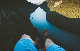 First-person view of hiker legs dangling over deep river gorge