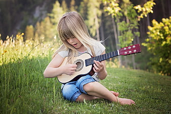 Young blonde girl playing acoustic guitar in grassy field