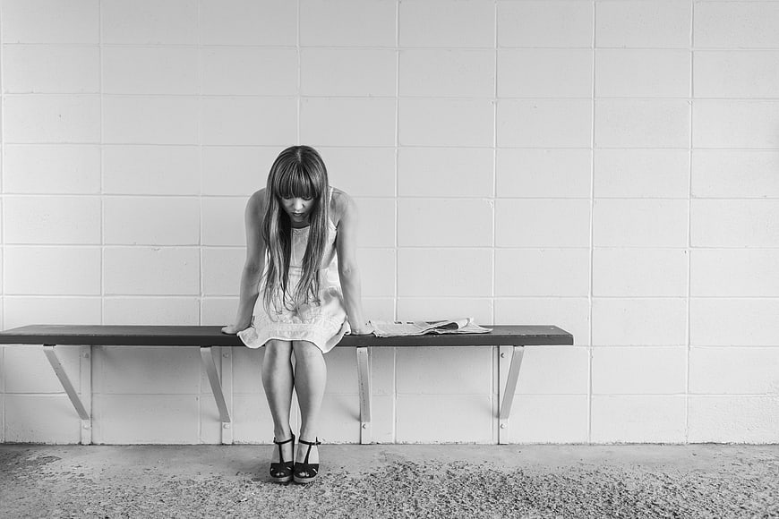 Sad woman sitting alone on bench against white wall