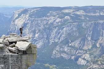 Hiker standing on rocky cliff edge overlooking vast mountain valley