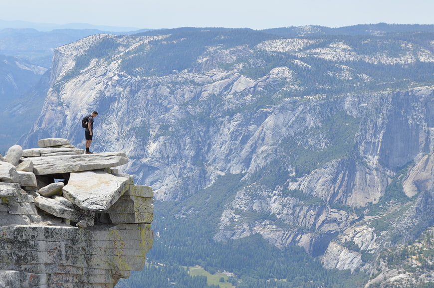 Hiker standing on rocky cliff edge overlooking vast mountain valley