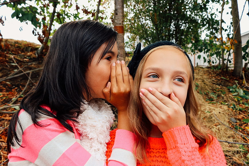 Two young girls whispering secrets outdoors in autumn