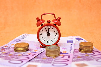 Red alarm clock on euro banknotes and coins