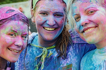 Three Smiling Women Covered in Colorful Powder at Festival