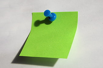 Green sticky note with blue push pin on white background