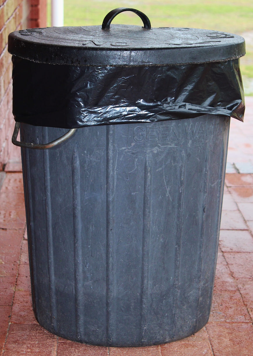 Black plastic garbage bin with lid on red brick patio