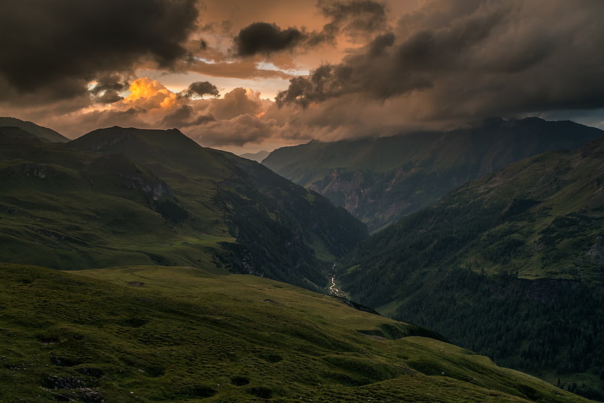 Dramatic mountain landscape with golden sunset light breaking through dark clouds
