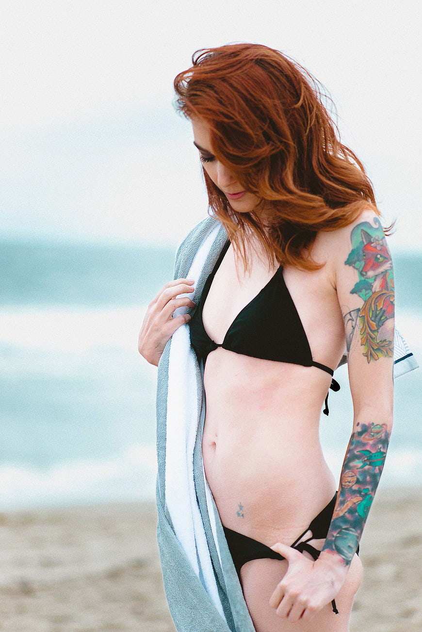 Redhead woman with tattoos in black bikini on beach
