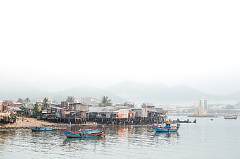Colorful fishing boats in a coastal village with stilt houses and foggy mountains
