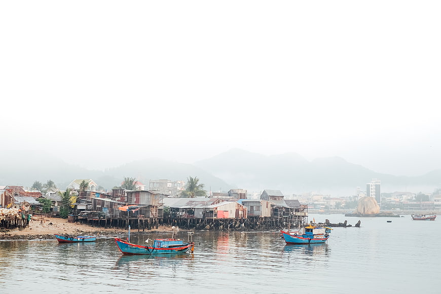 Colorful fishing boats in a coastal village with stilt houses and foggy mountains