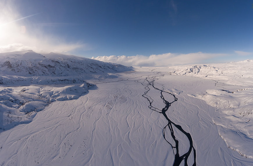 Aerial view of frozen river winding through snowy mountain landscape