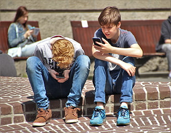 Two teenage boys playing mobile games on smartphones outdoors