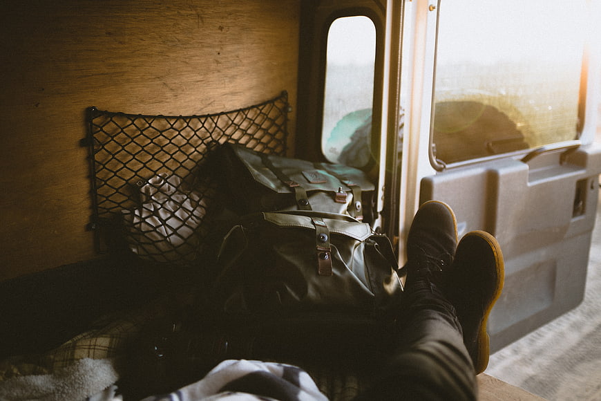 Relaxed traveler resting in van with bags and boots