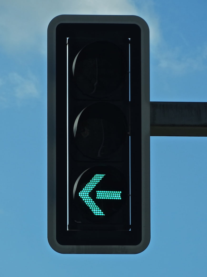 Green Left Arrow Traffic Light Signal Against Blue Sky