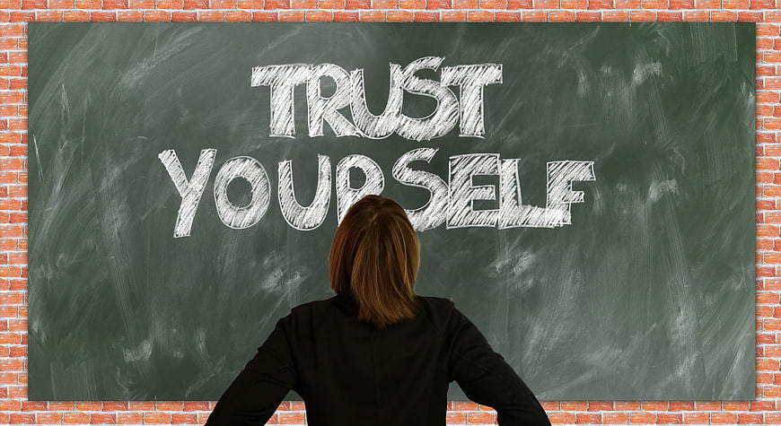 Woman looking at chalkboard with trust yourself written