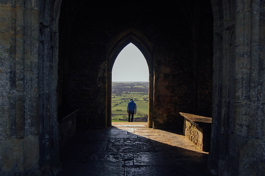 Man standing in stone archway looking at green countryside